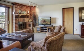 Living room with chairs, coffee table, brick wall fireplace, and tv.