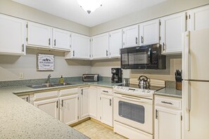 Kitchen with white cabinets and gray countertops. Appliances on counter and stove-top. Built-in microwave.