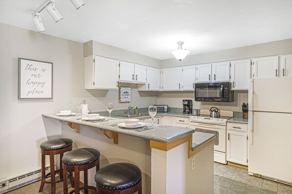 Kitchen with three stools at a gray counter. White cabinets with built-in microwave.