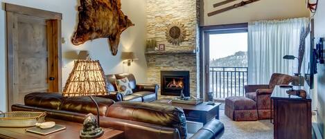 Rustic style living room with bear skin and skis hung on walls. Leather couches and featuring white brick fireplace.