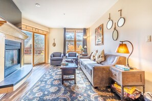 Living area with mounted flat screen TV, gas fireplace, balcony access, hardwood flooring and sleeper sofa.