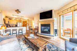 Living area with mounted flat screen TV, gas fireplace, balcony access, hardwood flooring and sleeper sofa.