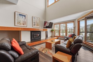Spacious living area with ample seating, vaulted ceilings, mounted TV, fireplace and access to the private balcony.