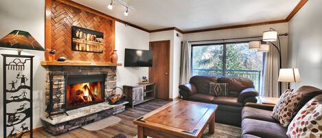 Cozy living room with wood burning fireplace, wall mounted TV, private patio
