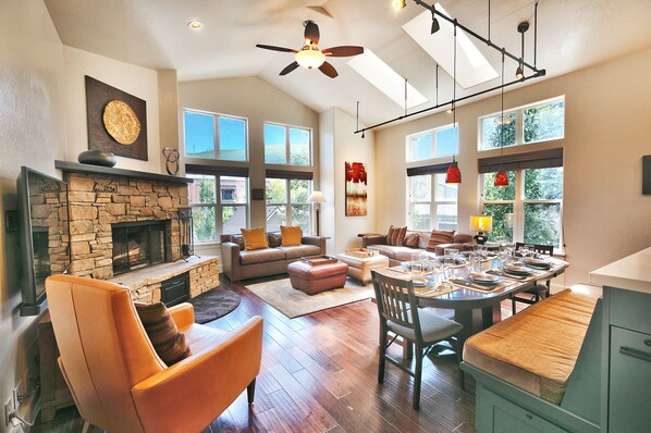 Bright open living room and dining room, abundant windows, stone fireplace and wall mounted large screen TV