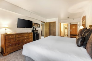 The main suite bedroom has a king size bed, white linens, wooden dresser and flat screen TV.