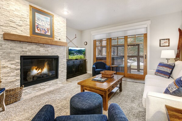 A cozy living room with a gas burning fireplace, flat-screen TV, cream couch and two blue club chairs.