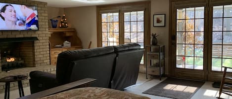 View from bed of TV, fireplace, couch, desk, the patio and woods. 