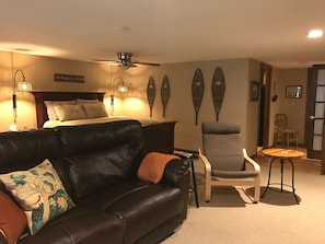 Double recliner couch, bed, & hallway that leads to walk-in closet & kitchen.