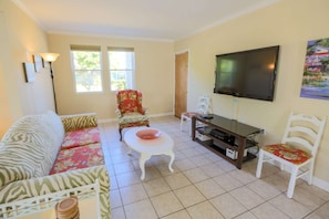 The living room of this pet friendly home features tiled floors, a large sofa and a large screen smart TV.