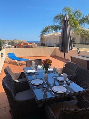 The outside alfresco dining area with a view of the pool terrace and the sea. 