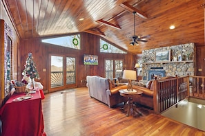 Main Living Area Features Large TV, Leather Seating, Floor to Ceiling Stone Fireplace, and Deck Access