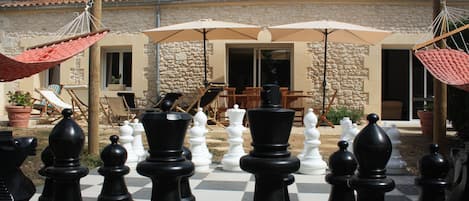 Extérieur de la maison avec grande terrasse, jeux d'échec géant entouré de ses hamacs rouges