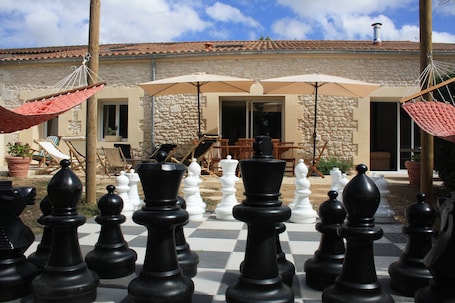 Extérieur de la maison avec grande terrasse, jeux d'échec géant entouré de ses hamacs rouges