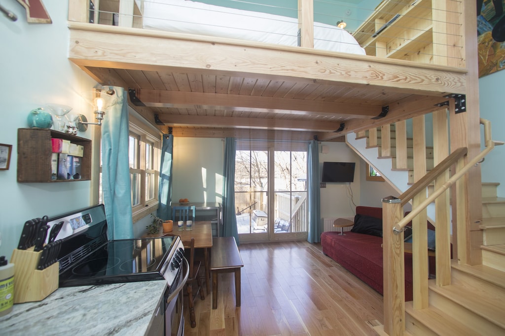A tiny house studio apartment in Burlington Vermont with light colored wood, a stove, a couch, and sliding glass door.