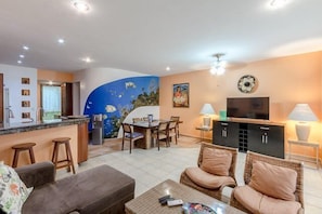 Large common area with dining table for six, flat-screen TV, and beautiful ocean mural