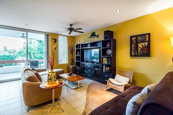 Living room has comfortable couches, a flat screen TV, and a balcony with ocean views