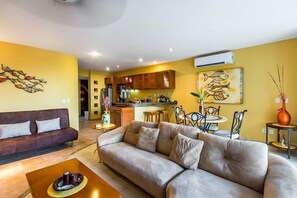 Living room has comfortable couches, a flat screen TV, and a balcony with ocean views