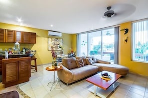 Living room has comfortable couches, a flat screen TV, and a balcony with ocean views