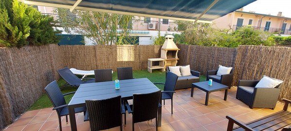Garden with armchairs, barbecue, table, awnings and sun loungers