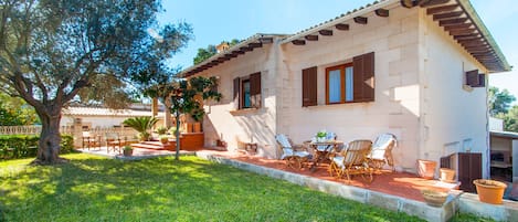 Outside lovely house with a garden and armchairs.