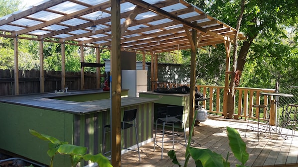 Outdoor kitchen has sink refrigerator ,microwave , bar seating, griddle