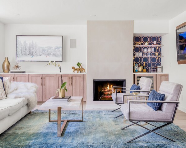 Modern and airy living room w/ wood-burning fireplace, custom cabinets and bar