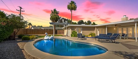 Large backyard featuring a covered patio with outdoor dining, fire pit with outdoor furnishings, heated pool, putting green, and a built-in BBQ and pizza oven.