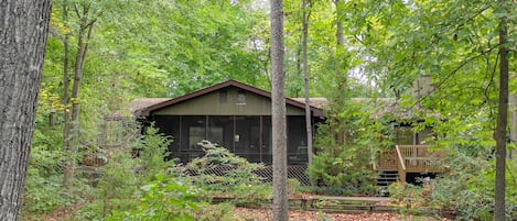 Nestled in the woods - view from lake to house. Deck on left of screen porch.
