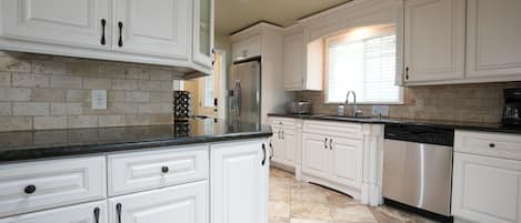 Kitchen with granite countertops, custom panel cabinetry with stainless steel appliances.