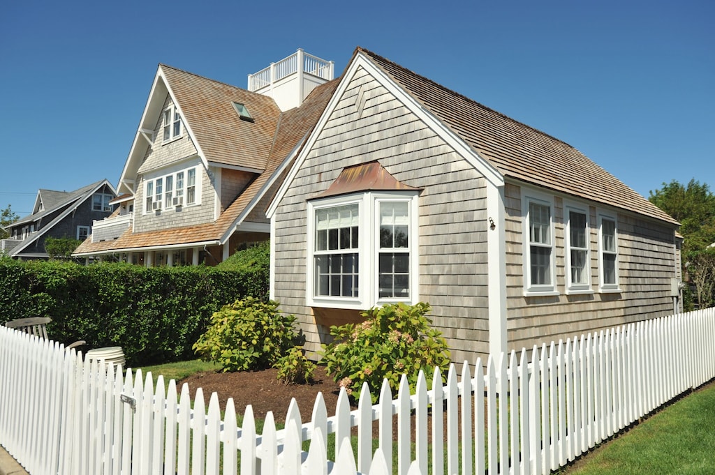 A small Nantucket cottage with a white picket fence on a sunny day