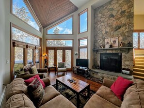 An open-concept layout with cozy furniture surrounds a massive stone wood-burning fireplace.
