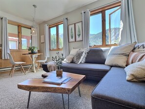 Chic Living Space: Our living room boasts a brand new sofa, plush pillows, a dinette set, and a 40-inch streaming TV, all framed by breathtaking mountain views. 