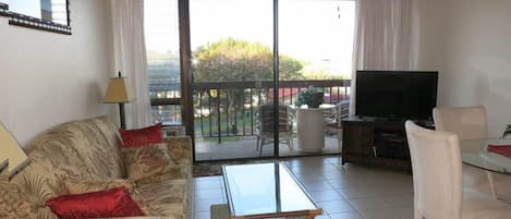 Living room with convertible sofa bed, dining table, flat screen TV, & lanai