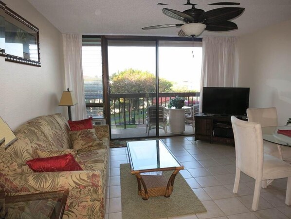 Living room with convertible sofa bed, dining table, flat screen TV, & lanai