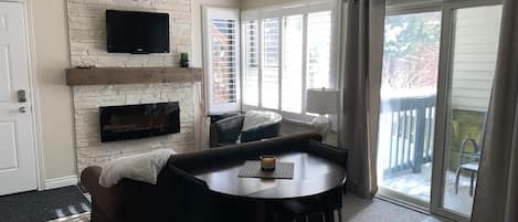 Main living area with electric fireplace and hillside view with evergreen trees!