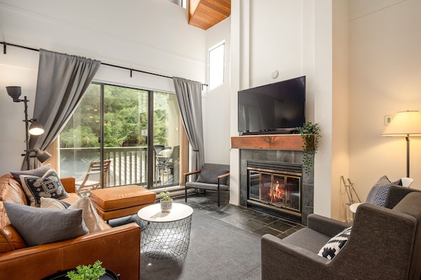 Living room w/ wood-burning fireplace and cable TV leading out to balcony w/ small Webber BBQ