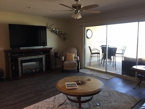 Main room with 6-seat dining, 2 barstools, 4-seat reclining sofa, electric fireplace, and 75” Roku Smart TV with Guest Mode, all overlooking the ocean.