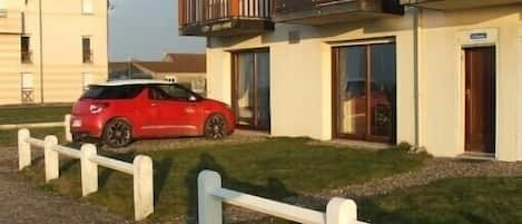 Vue du logement avec coin gazon devant et place de parking