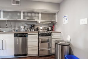 kitchen with oven/stove, dishwasher, garbage and recycling bins, and sink. 
