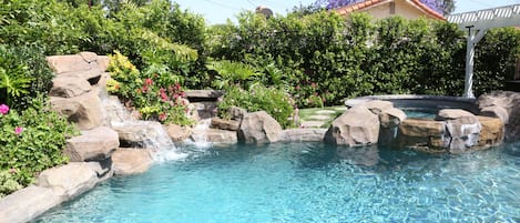 Beautiful Pebble-Tec Rock Pool with inground Jacuzzi. Raised walls stone work, and lighted waterfalls. The pool is surround by a scored concrete deck