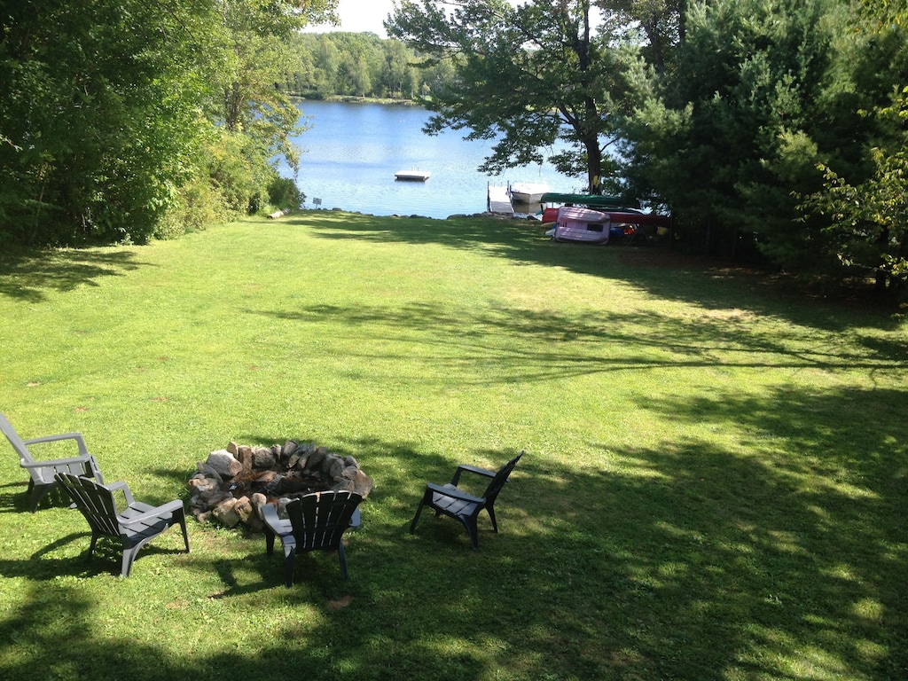 A large yard extends from a lakehouse rental on Lake Winnipesaukee clear down to the lake, with a firepit and chairs to enjoy by the water