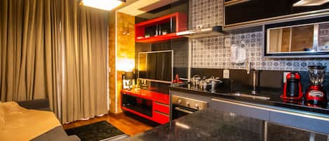 Sala decorada com detalhes em vermelho com televisão, cozinha completa.
