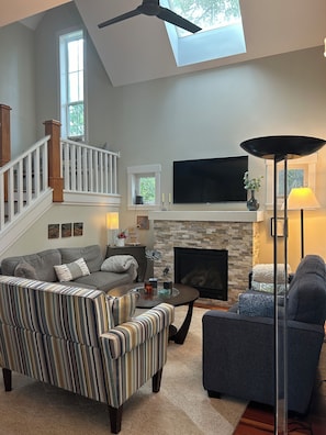 Bright living room with gas fireplace, ceiling fan, vaulted ceiling and skylight