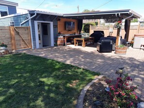 Outdoor covered patio area with propane fire pit, 2 couches, table, bbq & 65" TV