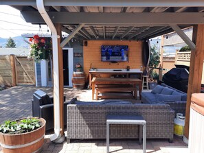 Outdoor covered patio area with propane fire pit, 2 couches, table, bbq & 65" TV