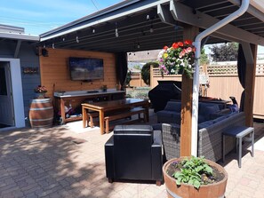 Outdoor covered patio area with propane fire pit, 2 couches, table, bbq & 65" TV