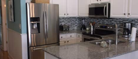 Kitchen with granite countertops, glass back splash & stainless appliances.