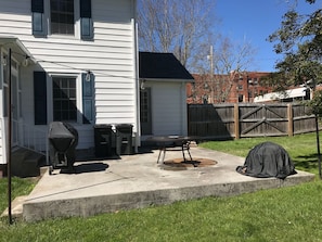 Back patio with grill, table and chairs and fire ring.