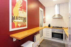 The kitchen features a breakfast bar with a single white stool, offering a convenient spot for enjoying a quick meal or a cup of coffee. The bar is positioned in front of a red wall adorned with a vintage poster. The kitchen itself is modern and well-equi